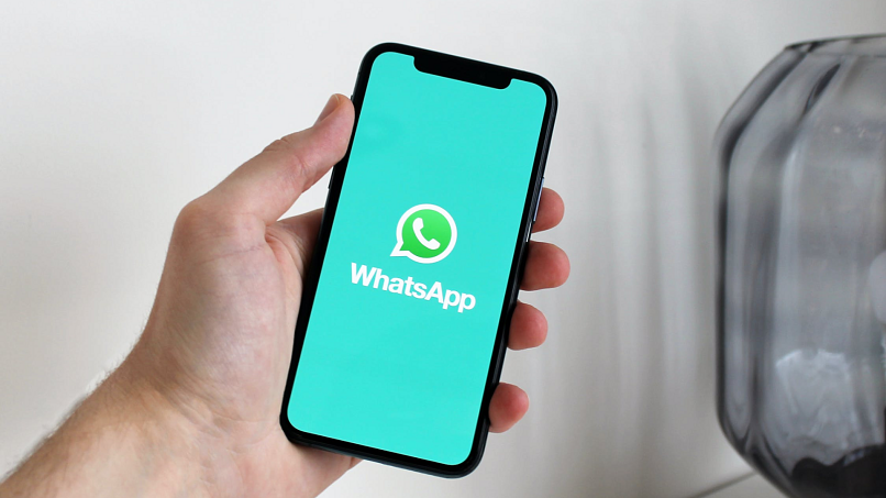 Image of the WhatsApp loading screen displayed on an iPhone held by a person