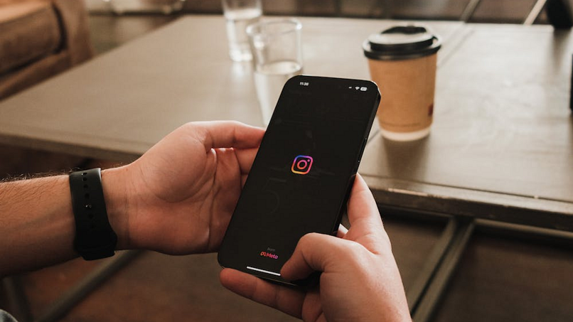 Image of a person in a coffee shop holding a phone showing the Instagram loading screen